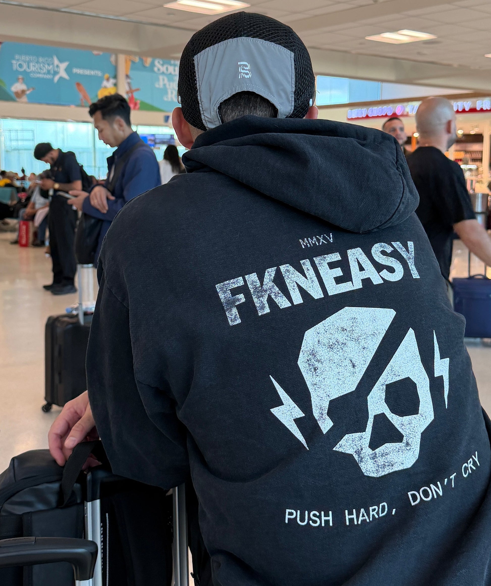 Person wearing a black hoodie with 'FKNEASY' branding in an airport setting