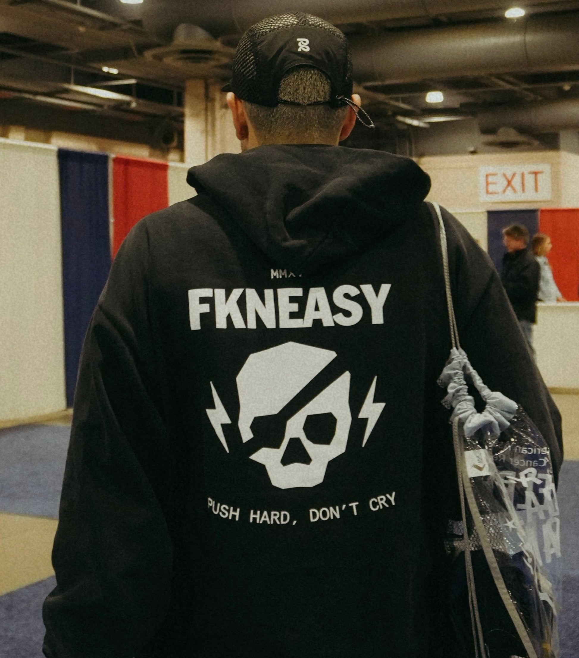 Person wearing a black hoodie with 'FKNEASY' branding in an indoor setting.